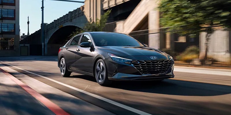 Gray Hyundai Elantra driving on a sunny city street.