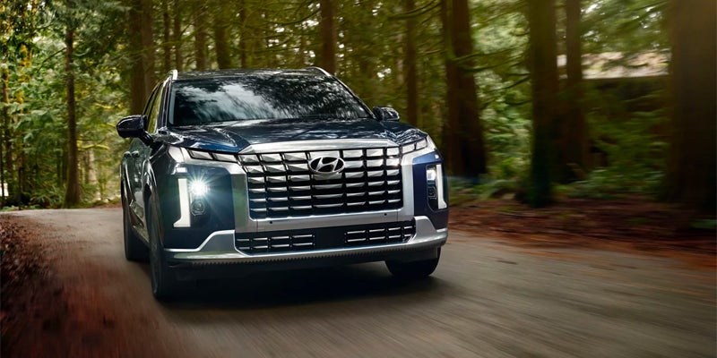Hyundai Palisade SUV driving on a wooded road surrounded by trees.