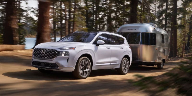 White Hyundai Santa Fe towing a camper trailer on a forest road.