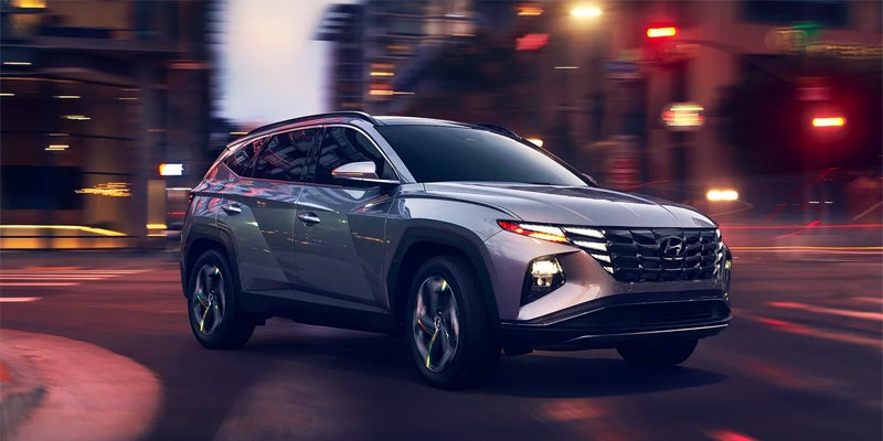 Hyundai Tucson SUV driving through a city street at night.
