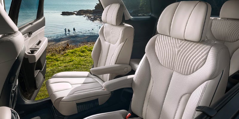 A car's interior shows plush, white seats and a view of a scenic shoreline through the open door.