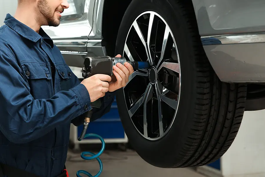 Technician performing tire maintenance and wheel service on a raised vehicle.