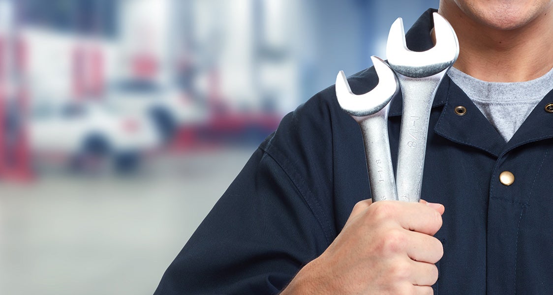 Service technician holding two wrenches in a repair shop.