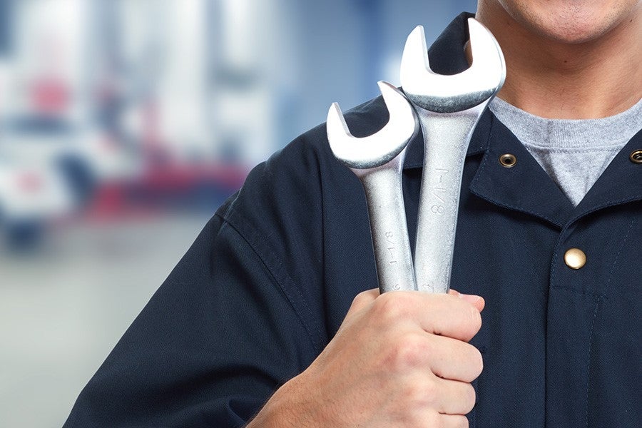 A mechanic holds a large wrench in his hand while wearing a gray uniform.